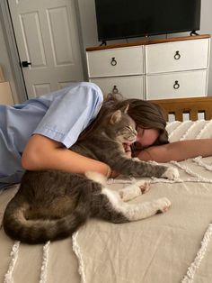 a woman laying on top of a bed next to a gray and white cat in her arms