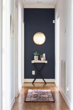 a hallway with blue walls and white trim, wooden flooring and a round mirror on the wall