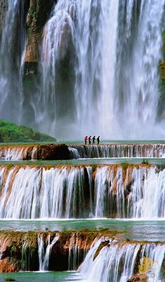 several people are standing at the base of a waterfall in front of water cascading