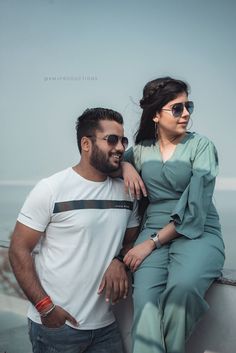 a man and woman posing for a photo on the side of a building near the ocean