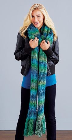 a woman wearing a blue and green knitted scarf with fringes on the ends