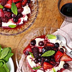 two desserts with berries, whipped cream and mint garnish sit on glass plates