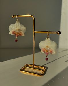 a pair of earrings with flowers hanging from it's hooks on a white surface