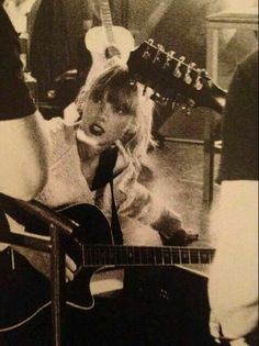 a black and white photo of a woman singing into a microphone while playing an acoustic guitar