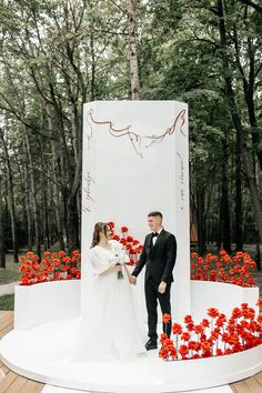 a bride and groom standing in front of a large sign with red flowers on it