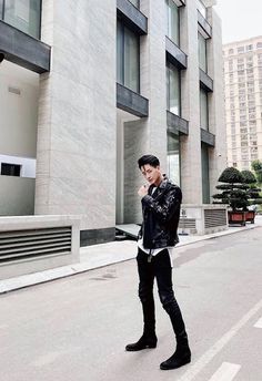 a man standing in front of a building talking on a cell phone while wearing black boots