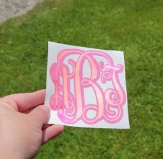 a person holding up a pink and white sticker with the letter b on it