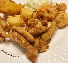 some fried food on a white plate with potatoes and coleslaw next to it