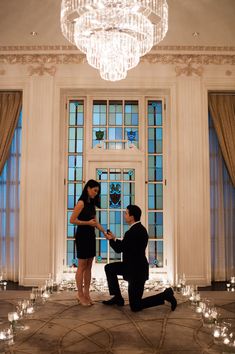 a man kneeling down next to a woman in front of a chandelier