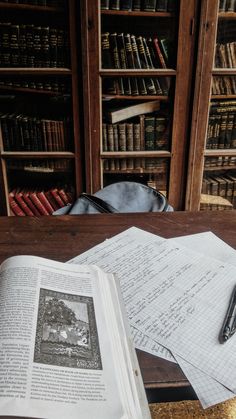 an open book sitting on top of a wooden table next to a pen and paper