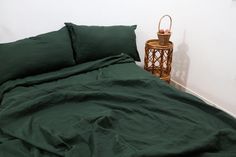 a bed with green sheets and pillows next to a small basket on the floor in front of it