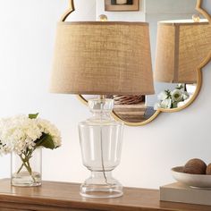 a table with a lamp, mirror and vase on it next to a flower arrangement