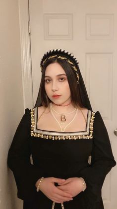 a woman wearing a black dress and headpiece standing in front of a white door