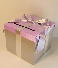 a pink and silver gift box with a bow on the top, sitting on a white surface