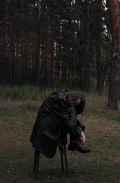 a person sitting on a chair in the middle of a forest with their head down