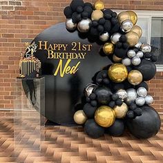 a black and gold balloon arch with the words happy 21st birthday next to it in front of a brick building