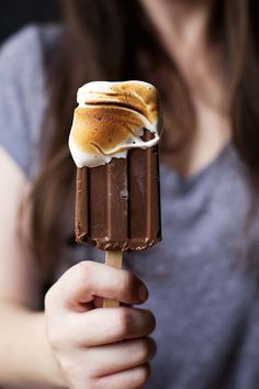 a woman holding a chocolate and marshmallow ice cream on top of a stick