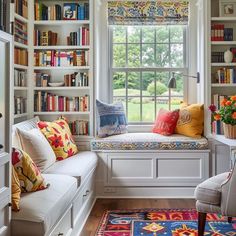 a room filled with lots of bookshelves next to a window covered in colorful pillows