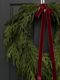 a christmas wreath hanging on a door with a red ribbon tied around it and a candle