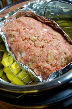 a meatloaf in foil sitting on top of a table next to pickles