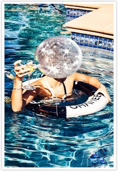 a woman floating in the water with a fan on her head and holding a drink