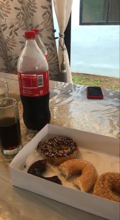 there are donuts in the box on the table next to a drink and cell phone