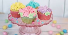 three cupcakes with colorful frosting and sprinkles on a cake plate