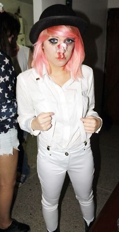 a woman with pink hair wearing white pants and a black hat is posing for the camera