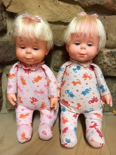 two little dolls are sitting next to each other on the floor in front of a stone wall