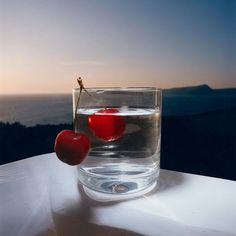 two cherries sit in a glass of water on a ledge overlooking the ocean at sunset