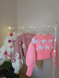 three knitted sweaters are hanging on a clothes rack with lights in the background