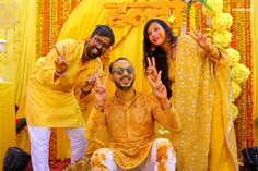 two men and a woman posing for a photo in front of a yellow backdrop with flowers