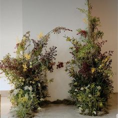 an arch made out of branches and flowers on the floor in front of a wall