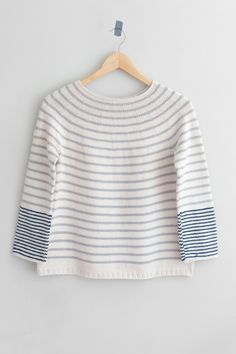 a white and blue striped sweater hanging on a wooden hanger, with the top half turned down