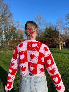 a woman standing in the grass wearing a red and white crochet heart sweater