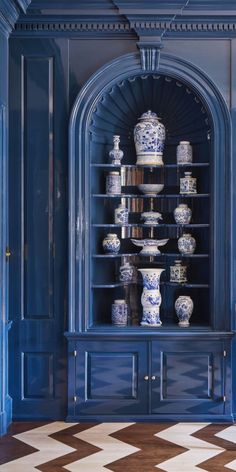 a chair sitting in front of a blue book shelf filled with vases and bowls