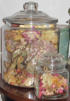 a glass jar filled with dried flowers sitting on top of a wooden table next to a vase