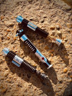 two pens laying on top of each other in the sand next to rocks and gravel