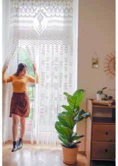 a woman standing in front of a window next to a potted plant