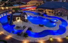 an aerial view of a backyard with a pool and fire pit at night, lit up by lights