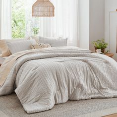 a bed in a bedroom next to a window with white drapes and pillows on it