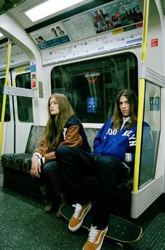 two young women sitting on a subway car with their skateboards in front of them