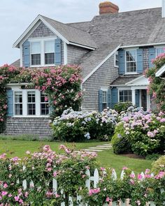 a house that has some flowers in front of it and bushes around the yard area