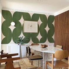 a dining room with green and white wallpaper, chairs and a marble table in the center