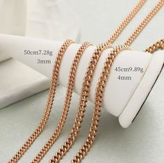 four different types of gold chains on a white table next to a roll of paper