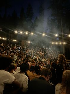 a large group of people sitting in front of a stage with lights on the ceiling