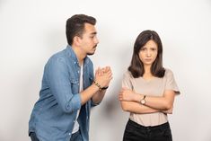 two people standing next to each other in front of a white wall with their arms crossed