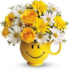 a smiley face vase filled with yellow and white daisies, roses and other flowers