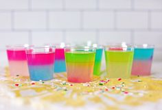 there are four glasses with different colors on the table and sprinkles around them