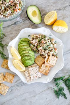 a white plate topped with crackers, cucumber and other food next to lemon wedges